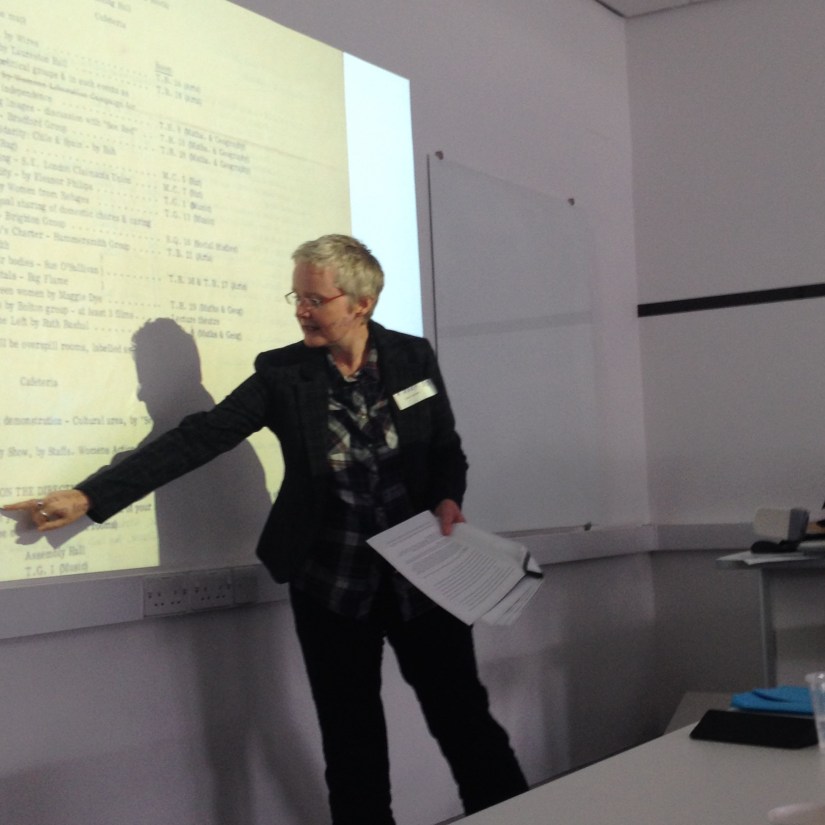 Julie at front of a room pointing to something on a powerpoint slide.