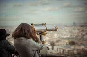 woman looking through a telescope at a city landscape
